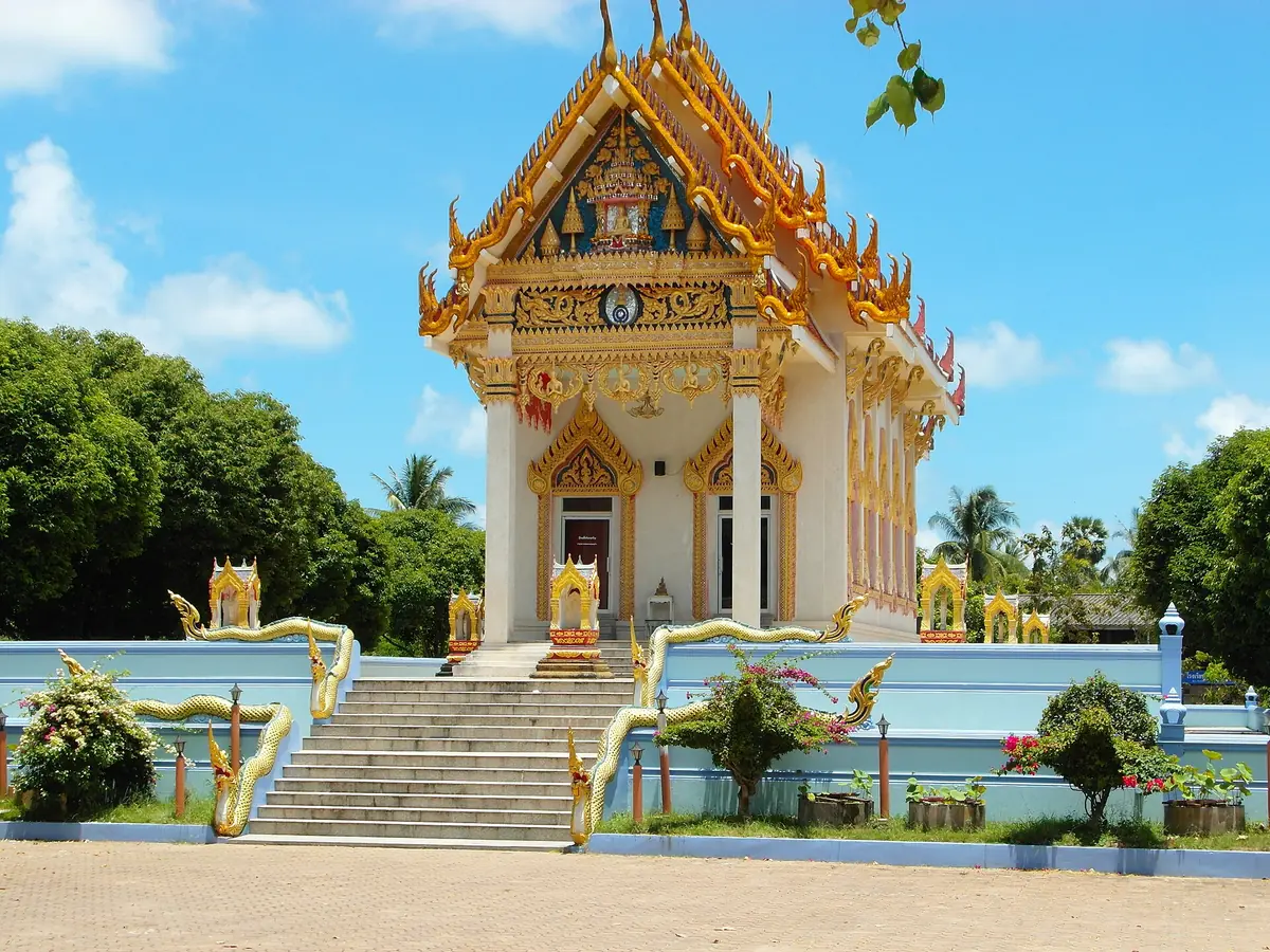 Thai temple hall with gilded gables, a staircase flanked by naga serpents and palms around it