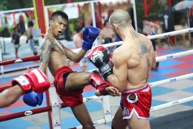 Two fighters in red silk shorts sparring in an open air ring in daylight