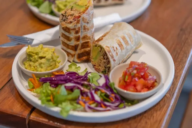 A plate with two halves of a filled tortilla, guacamole, salsa and cabbage salad