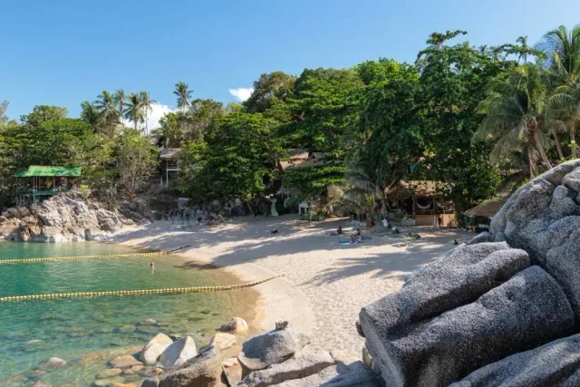 A small cove with giant boulders, a yellow buoy chain and huts among the trees