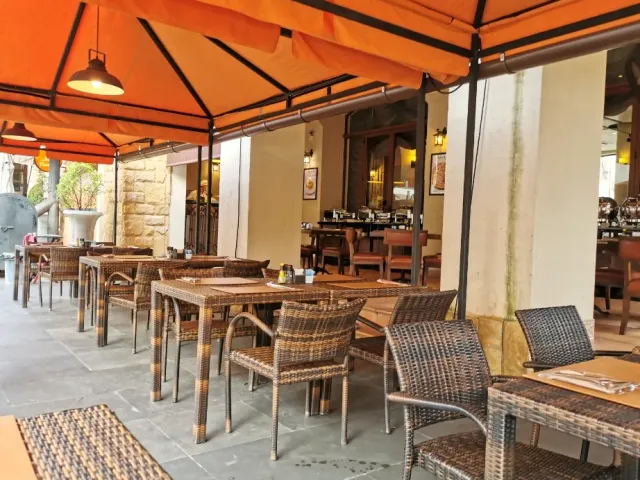 A paved terrace with orange awnings, woven chairs and a stone wall to the side