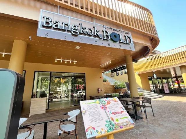 A restaurant facade in an open air shopping center, tables outside and a sign above the entrance