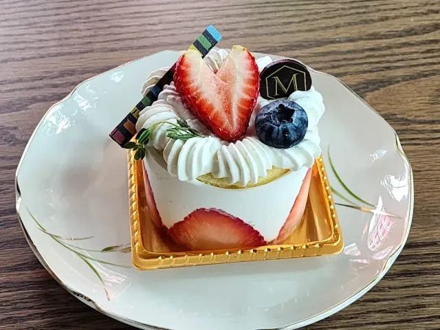 A small cream cake with a halved strawberry, a blueberry and a rosemary sprig on a plate