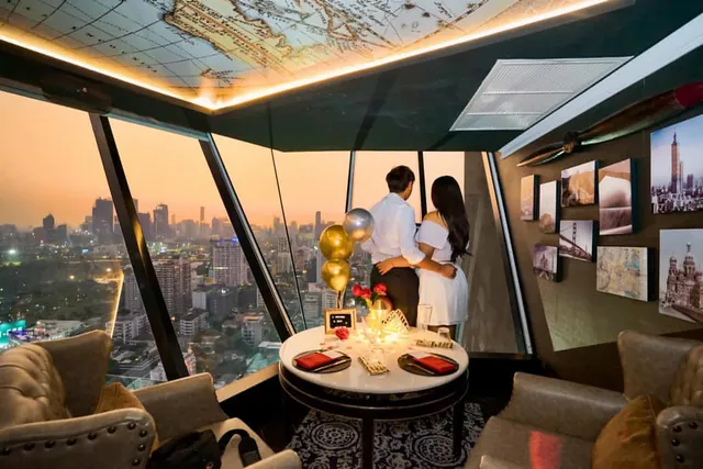 An embracing couple facing slanted windows overlooking the city, beside a set table with balloons