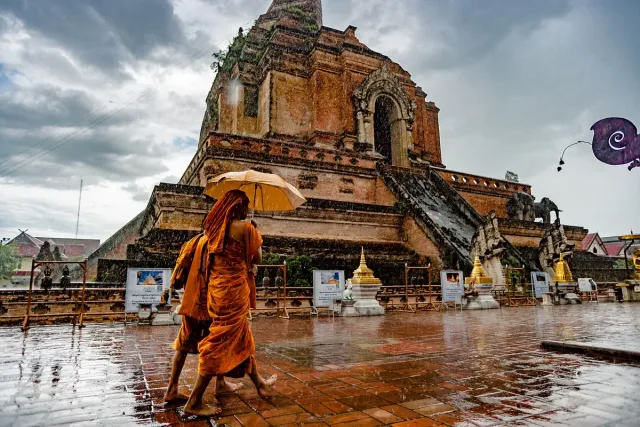 A huge brick chedi with elephant figures at its base, monks crossing a rain soaked courtyard