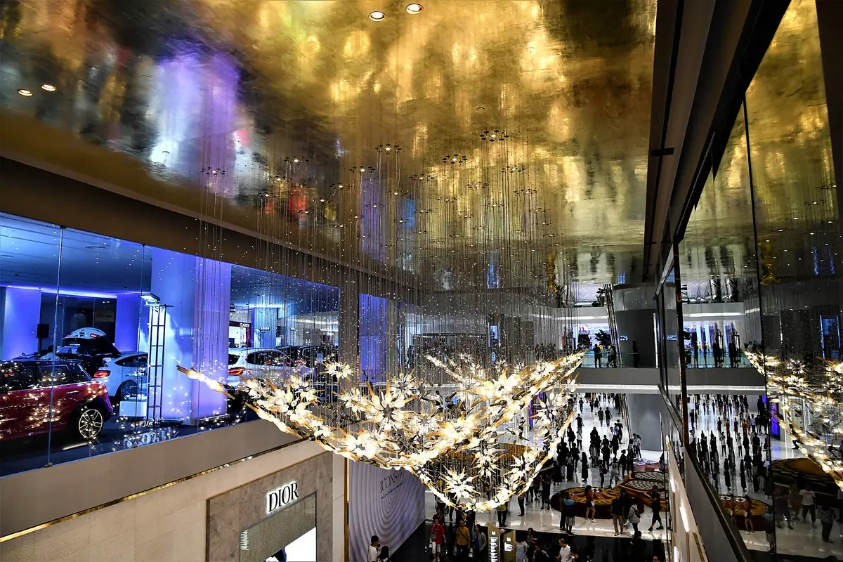 A vast shopping atrium with a golden ceiling, a branching crystal chandelier and floors full of visitors