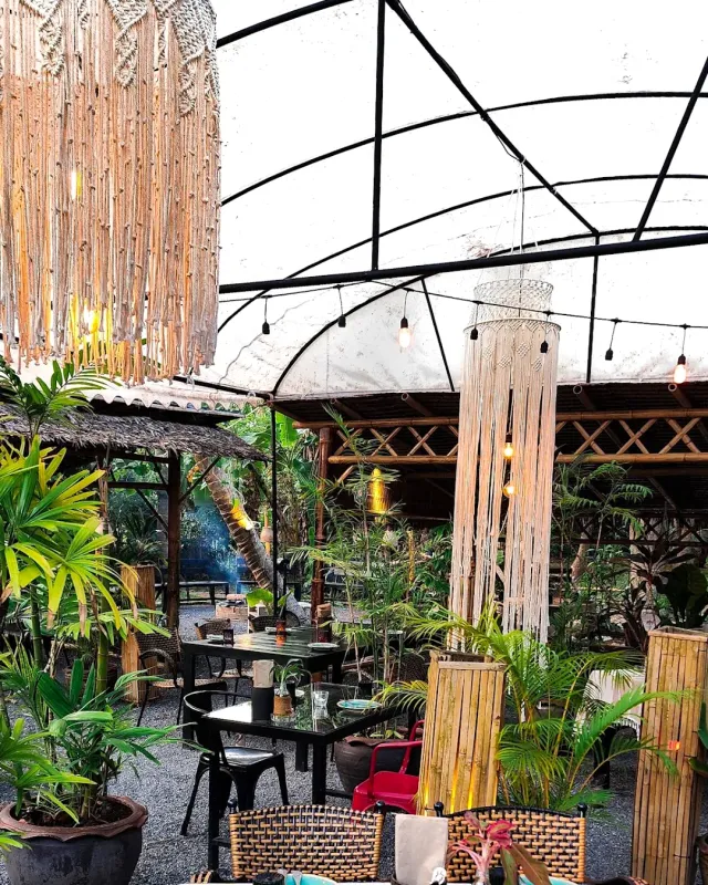 A garden patio with hanging rope chandeliers, black tables and tropical greenery around