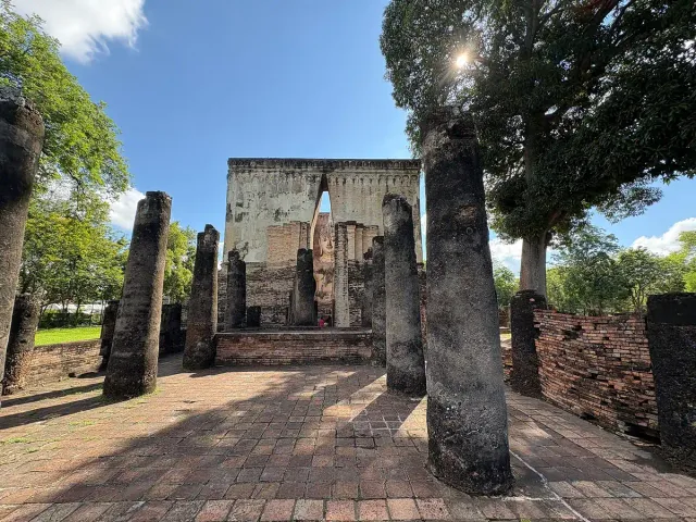 A tall stone structure with a narrow slot revealing a gilded figure, among stone columns and ruins