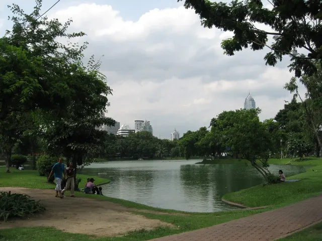 A calm lake in a city park with lawns, trees and skyscrapers on the horizon