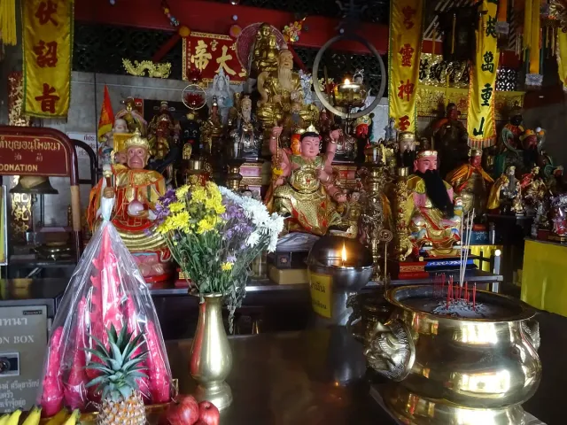 A Chinese altar crowded with colorful deity statues, a brass incense burner and fruit offerings