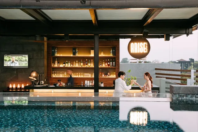 A rooftop pool beside a bar counter, with a couple raising glasses across the water