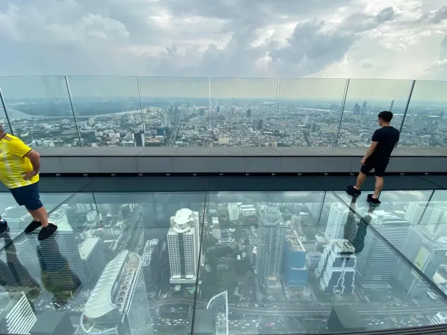 A glass floor at the top of a skyscraper and two visitors above the city towers