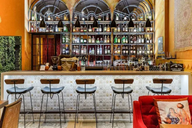 A drinks counter with arched shelves full of bottles, stools and a red sofa to the side