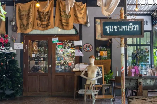 A facade with hanging burlap sacks, a wooden door covered in stickers and a Thai sign