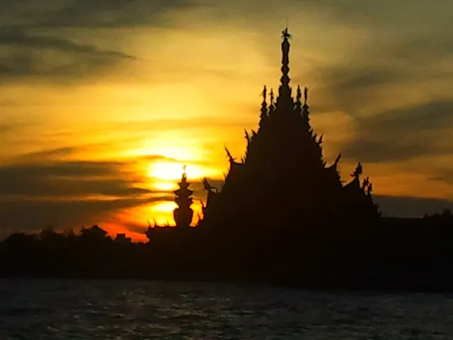 The silhouette of a spired, heavily carved wooden building against an orange sunrise sky