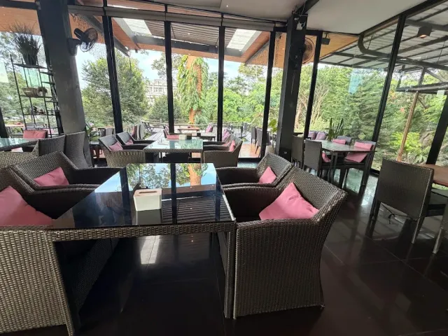 A space with glass walls, rattan armchairs and pink cushions facing green foliage
