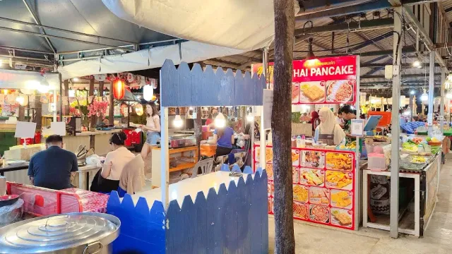 Food stalls under tents in the evening, a blue wooden fence and photo menus