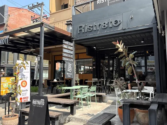 A black street facade with mint chairs, sidewalk tables and menu signs