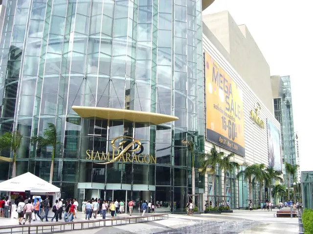 The curved glass frontage of a large shopping centre with palms and visitors at the entrance