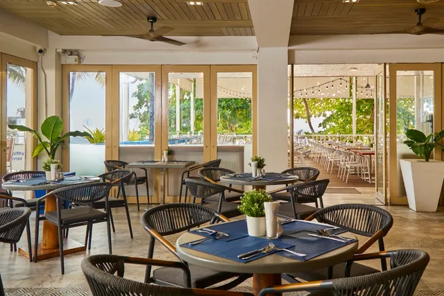 A restaurant hall with set tables and glass doors opening onto a green terrace