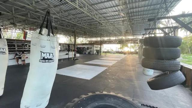 An open air training hall with hanging punching bags, tires and mats on the floor