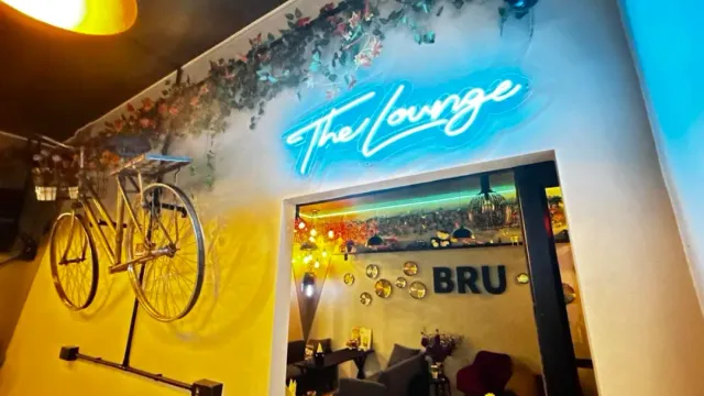 A light blue neon sign on the wall, a golden bicycle hanging and an opening to a seating space