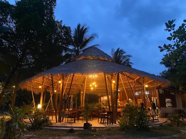 A round pavilion with a thatched roof and warm lighting among palm trees at dusk