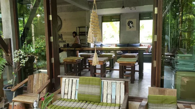 An open space with wooden stools and triangular cushions, and a long table facing windows onto the garden