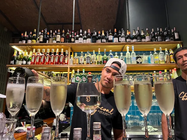 A bartender pours wine into a row of glasses in front of lit bottle shelves