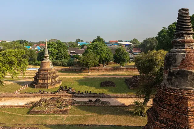 A high view over brick chedis and the lawns of a ruined temple compound with the town behind