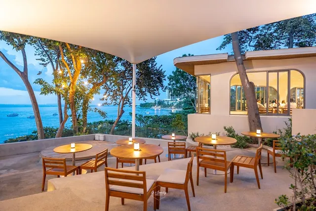 A terrace with wooden tables and candles under an awning, facing a bay at dusk