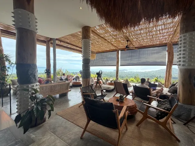 A thatched lounge with wooden armchairs and a round table and an open sea view