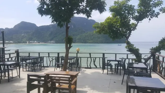 A seaside terrace with tables, a tree in the middle and green cliffs behind