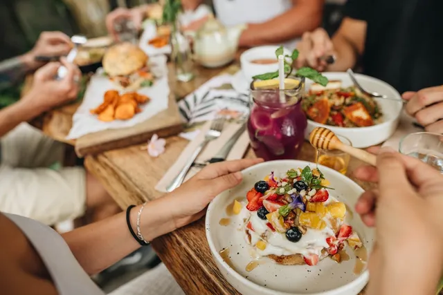 A wooden table full of brunch dishes, fresh fruit and a purple drink