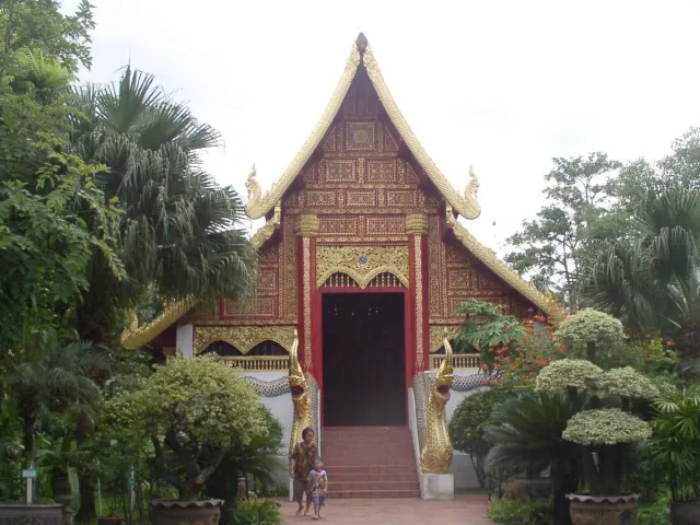 A wooden temple hall with tiered roofs and gilded trim among trees and tended gardens