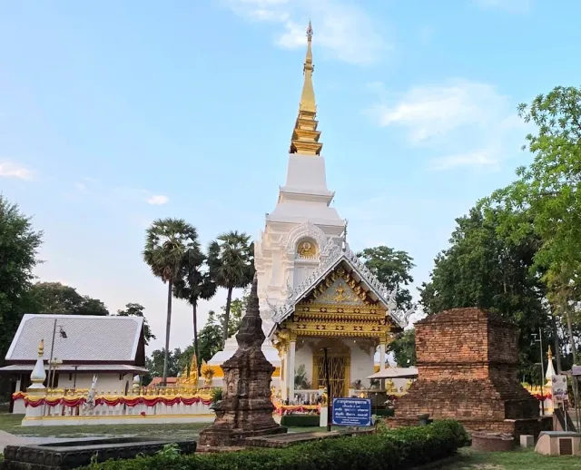 A white chedi with a gilded spire, brick ruins and palms in the background