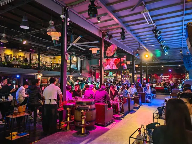 A large hall in pink and blue lighting, barrel tables and a big crowd