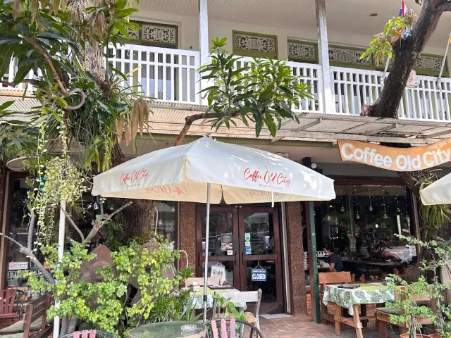 White parasols in front of a white wooden balcony, outdoor tables and green trees