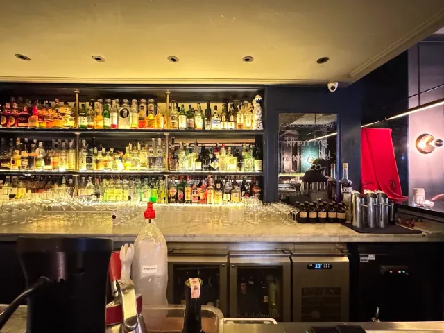 A lit wall of bottles behind a marble counter, hanging glasses and wine fridges
