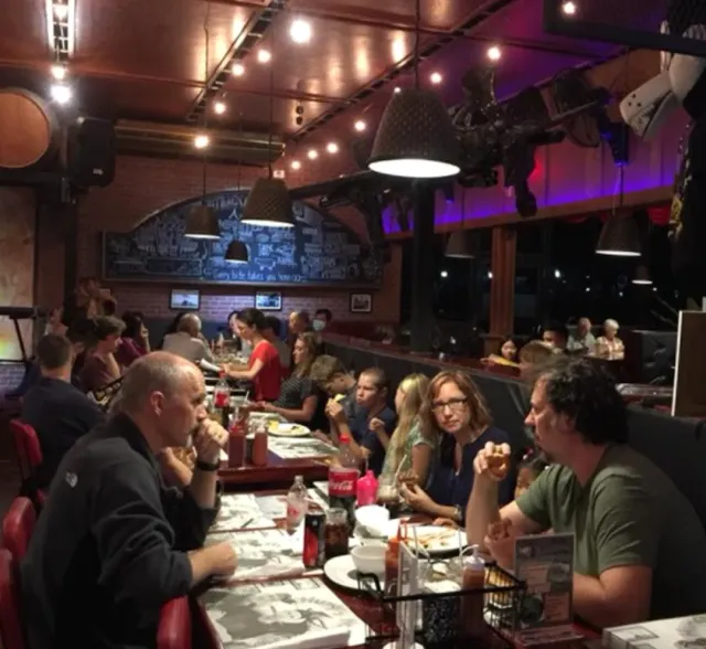 A long table full of diners in a red brick space with a chalkboard and warm lighting