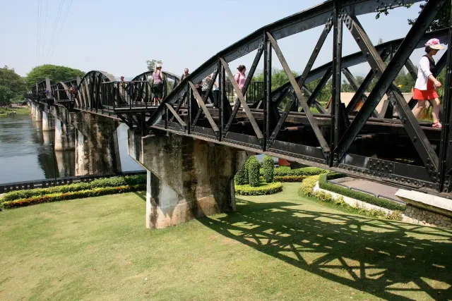 A black steel railway bridge spanning a wide river between green banks