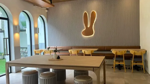 A ribbed wall with a lit rabbit ears emblem, a long bench and yellow stools