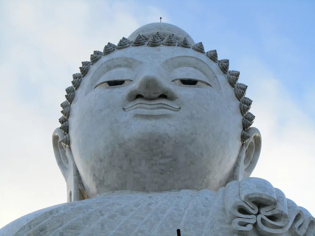 The face of a giant white marble Buddha, shot from below against a pale sky