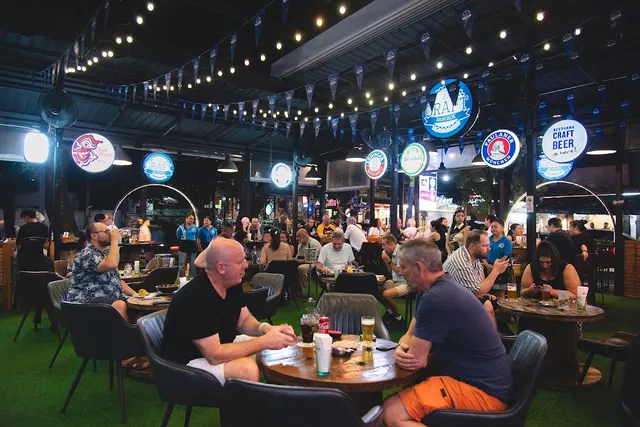 People with glasses of beer around round tables on artificial grass, under strings of bulbs