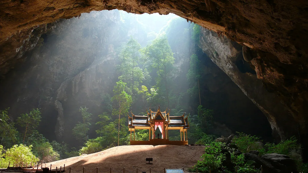 A gilded pavilion standing on the floor of a huge cave, in a shaft of light falling from the ceiling opening