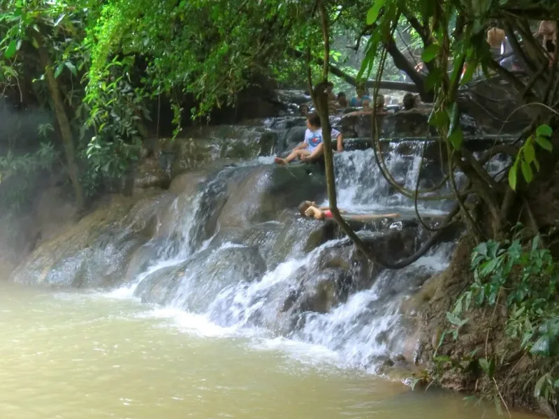 Bathers sitting in the terraced pools of the Krabi hot spring waterfall, surrounded by jungle