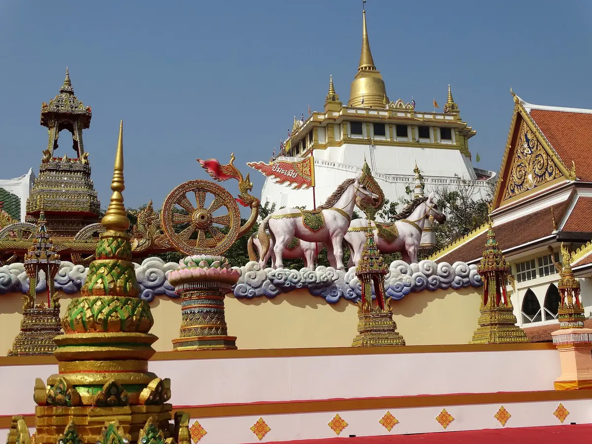 A gilded chedi on an artificial hill, above white horse sculptures and ornate spires