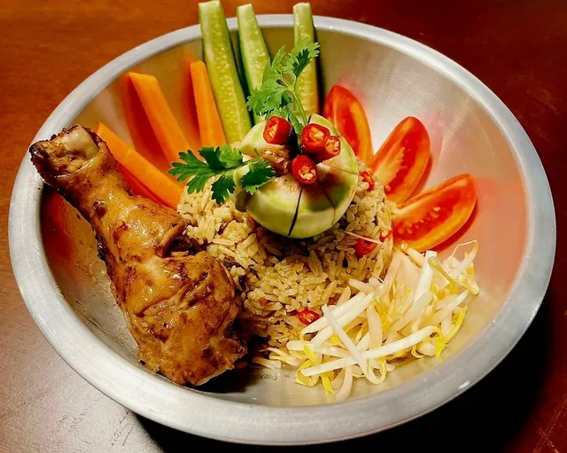 A metal bowl with rice, a roasted chicken drumstick, bean sprouts and fresh vegetables