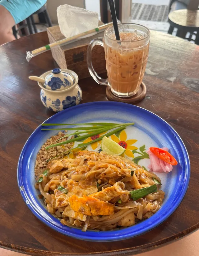 Stir-fried noodles on a blue plate beside a glass of iced milk tea