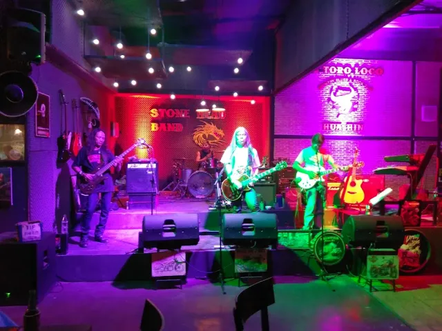 A band playing on stage in purple and green lighting, guitars and a drum kit